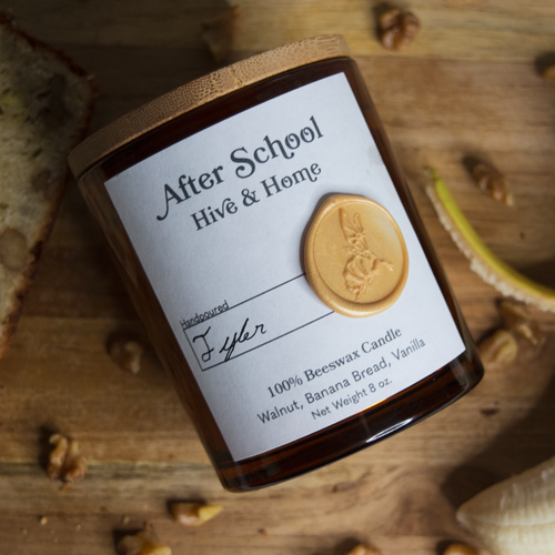 Flat lay of our apothecary beeswax candle surrounded by slices of fresh walnut banana bread, chopped walnuts, and a peeled banana on a wood background