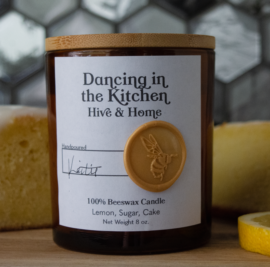Dancing in the Kitchen candle in front of a fresh lemon pound cake loaf and slices, and a fresh lemon slice.