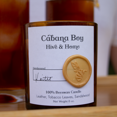 The Cabana Boy candle on a bamboo tray in front of two drinks, held by a cabana boy.